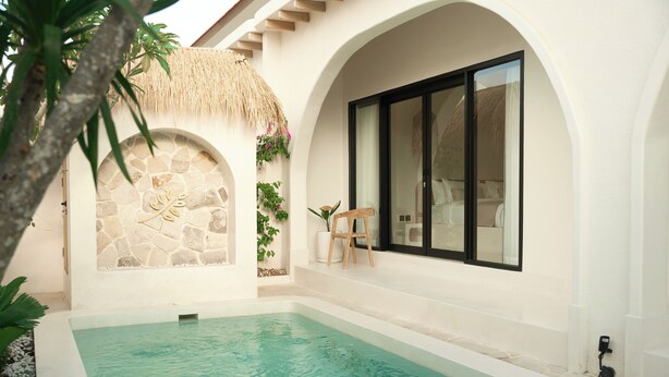 Zona de piscina con pared de piedra, techo de paja y una silla de madera.