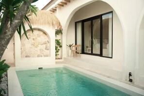 Zona de piscina con pared de piedra, techo de paja y una silla de madera.