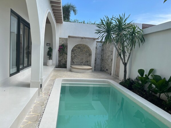Una piscina con borde de piedra, muro de piedra y una palmera.