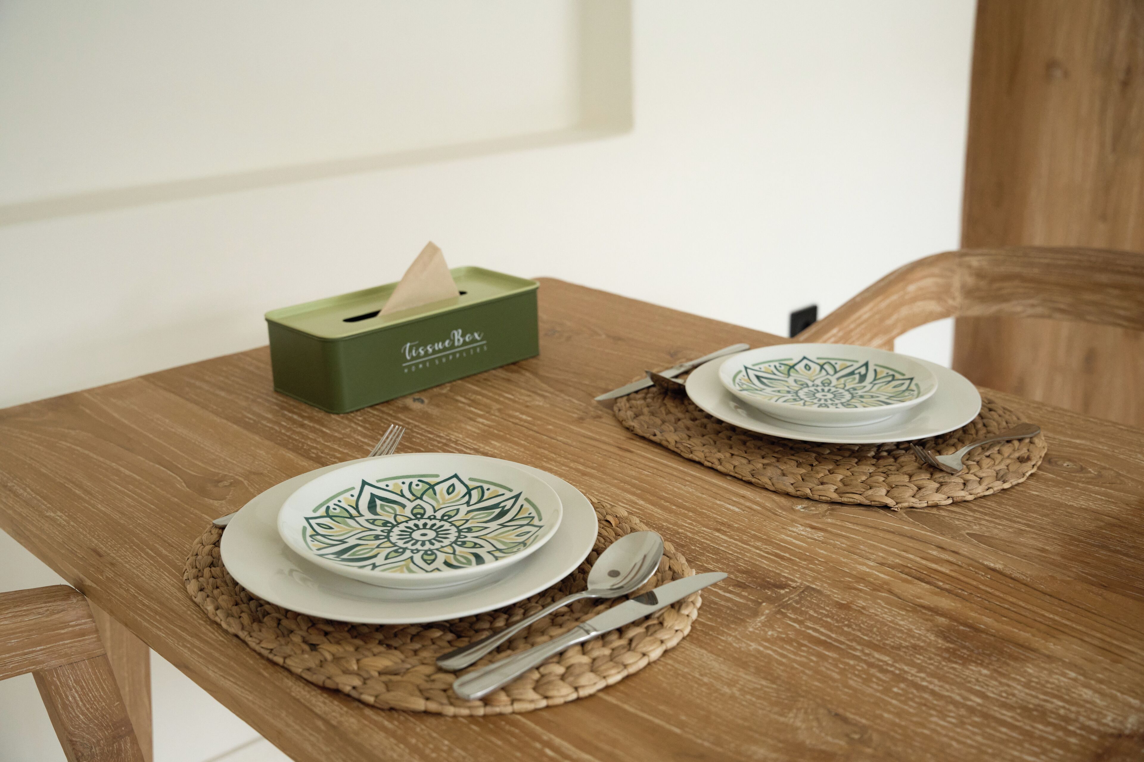 A wooden dining table with two plates, cutlery, and a tissue box.