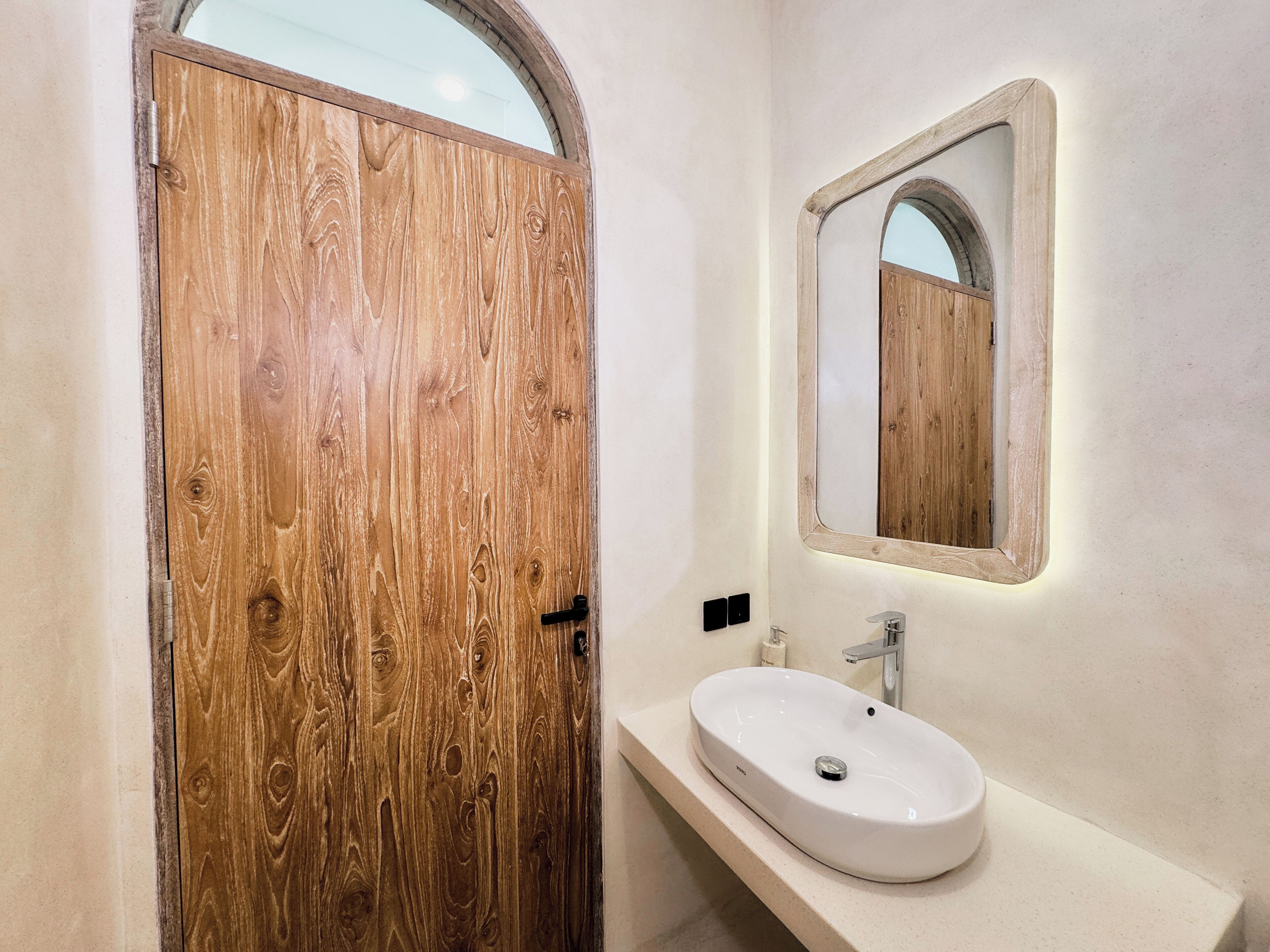 A wooden door with a mirror above a white sink in a bathroom.