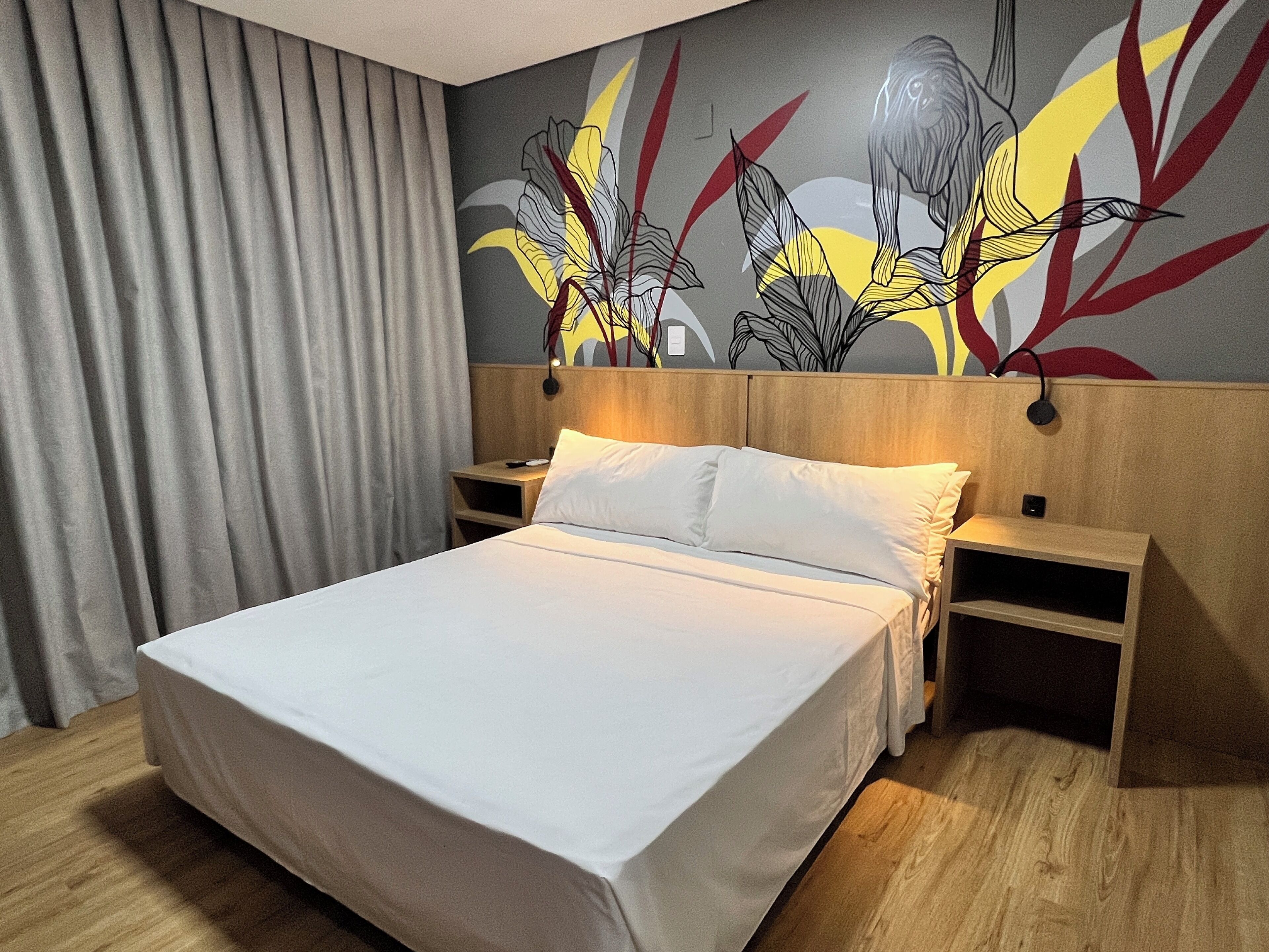 Una habitación de hotel con cama, cabecera de madera, mesitas de noche y un mural floral en la pared.