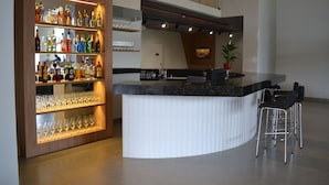 A modern bar area with a curved counter, multiple shelves of liquor bottles, and a few stools. - Ramada Encore Ponta Grossa  (Ponta Grossa)
