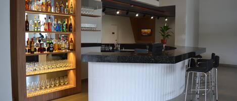 A modern bar area with a curved counter, multiple shelves of liquor bottles, and a few stools.