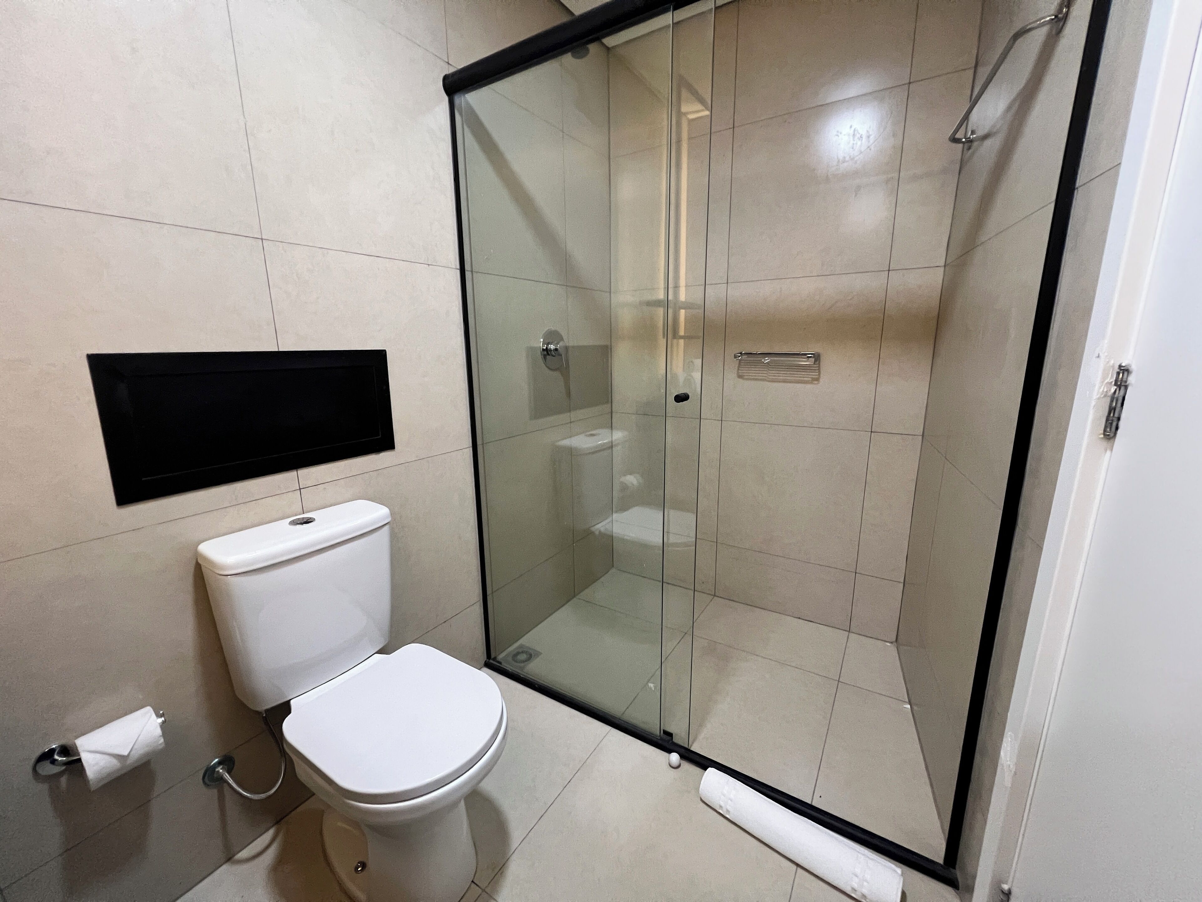 A bathroom with a toilet, a glass-enclosed shower, and a wall-mounted TV.