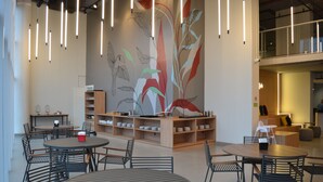 A modern interior with round tables and chairs, a mural with abstract plant designs, and a wooden shelving unit with dishes. - Ramada Encore Ponta Grossa  (Ponta Grossa)