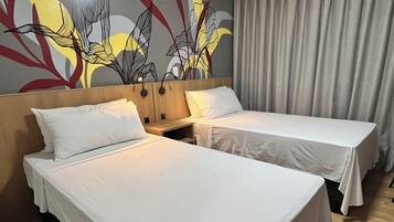 Quarto de hotel com duas camas de solteiro, cabeceira de madeira, painel decorativo na parede e cortina cinza.