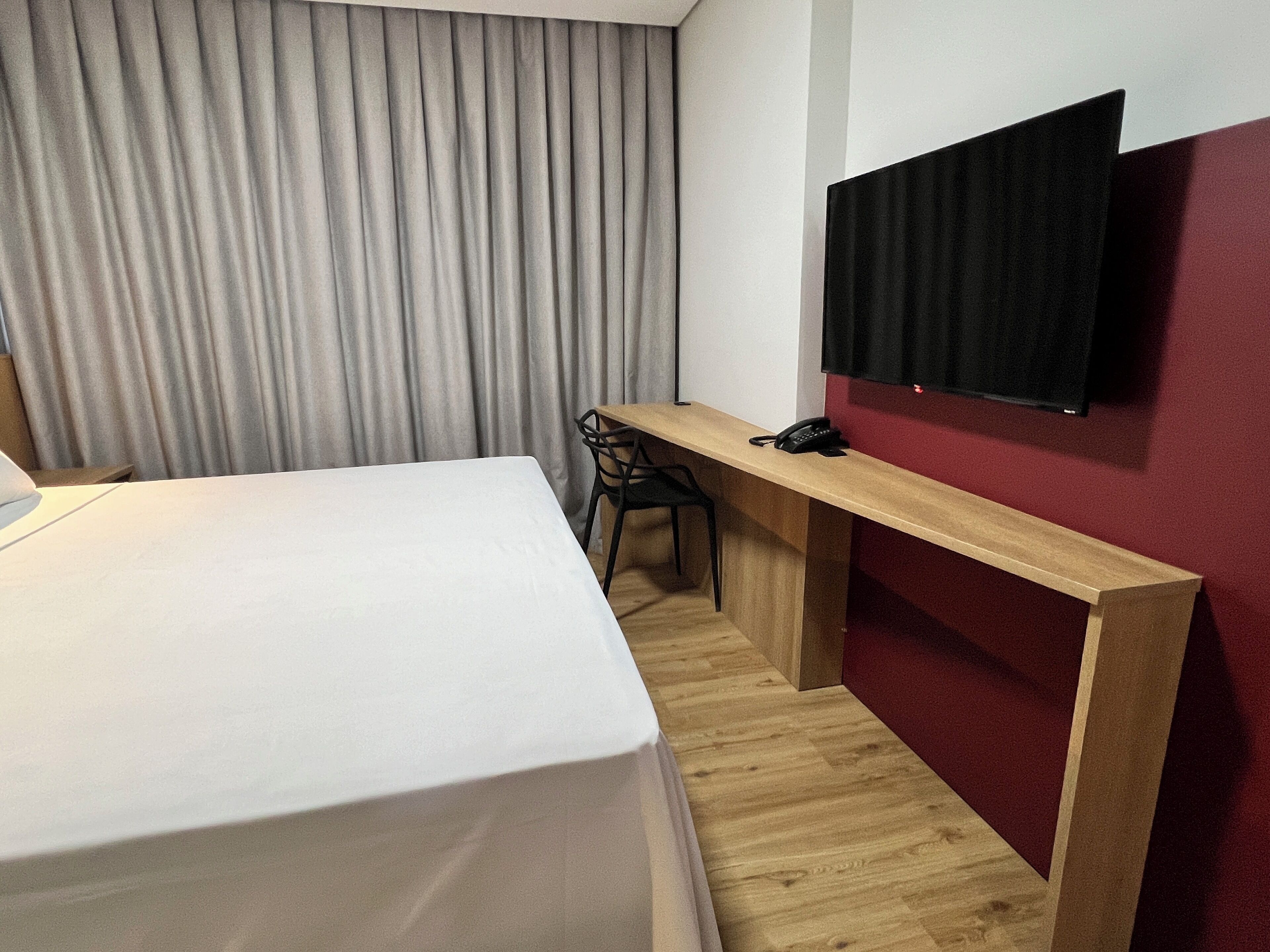 Habitación de hotel con cama, escritorio, silla, teléfono y televisor montado en la pared.