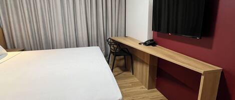 Habitación de hotel con cama, escritorio, silla, teléfono y televisor montado en la pared.