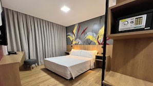 A modern hotel room with a large bed, wooden flooring, a desk, a chair, a nightstand, a wall-mounted TV, and a minibar. - Ramada Encore Ponta Grossa  (Ponta Grossa)