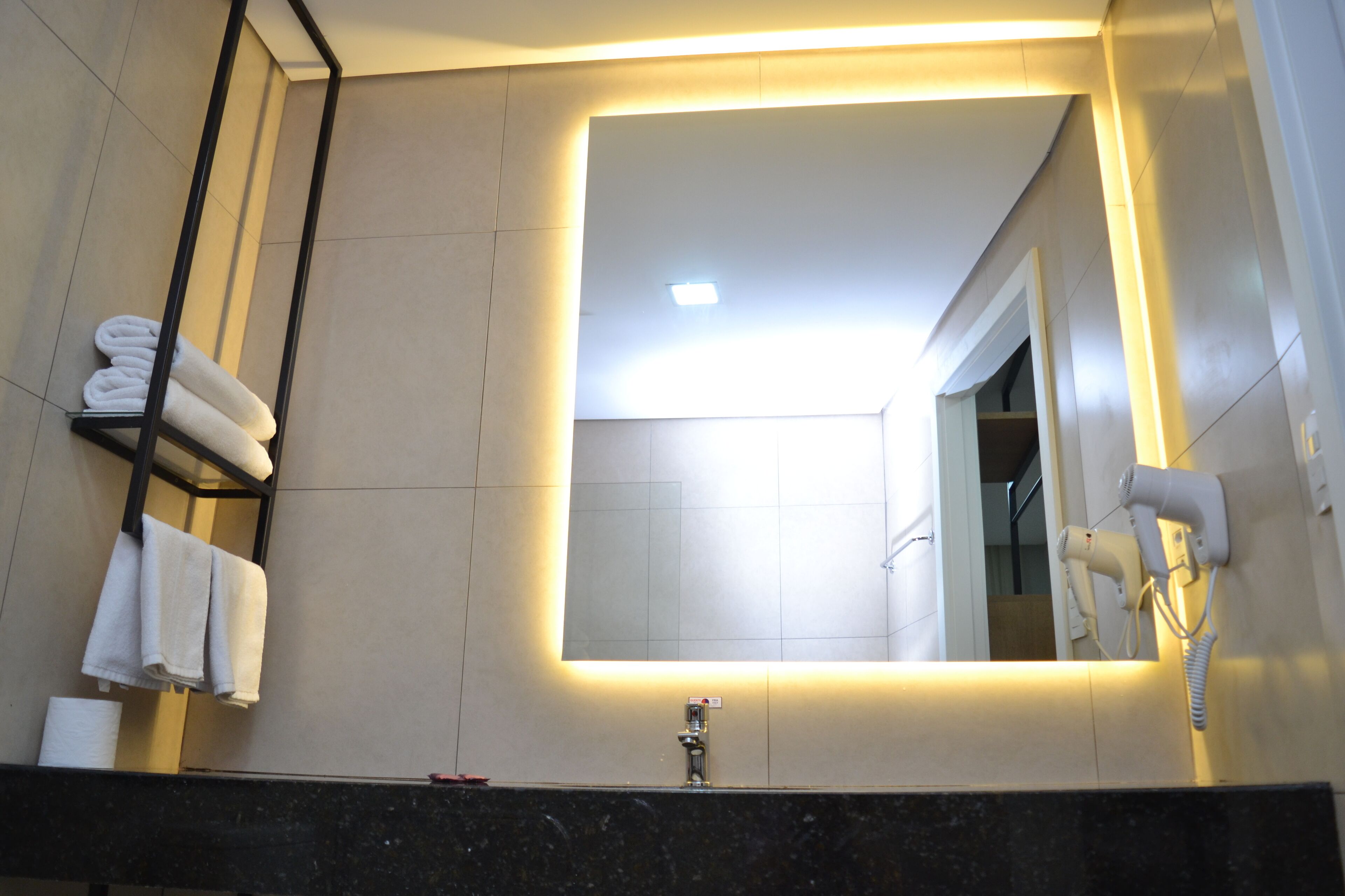 A modern bathroom with a large mirror, a towel rack, a hairdryer, and a sink.