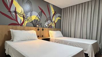 Habitación de hotel con dos camas, cabecero de madera, un mural en la pared y cortina gris.