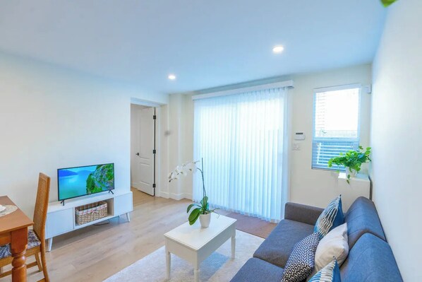 A modern living room with a flat-screen TV, a sofa, a coffee table, and a potted orchid.