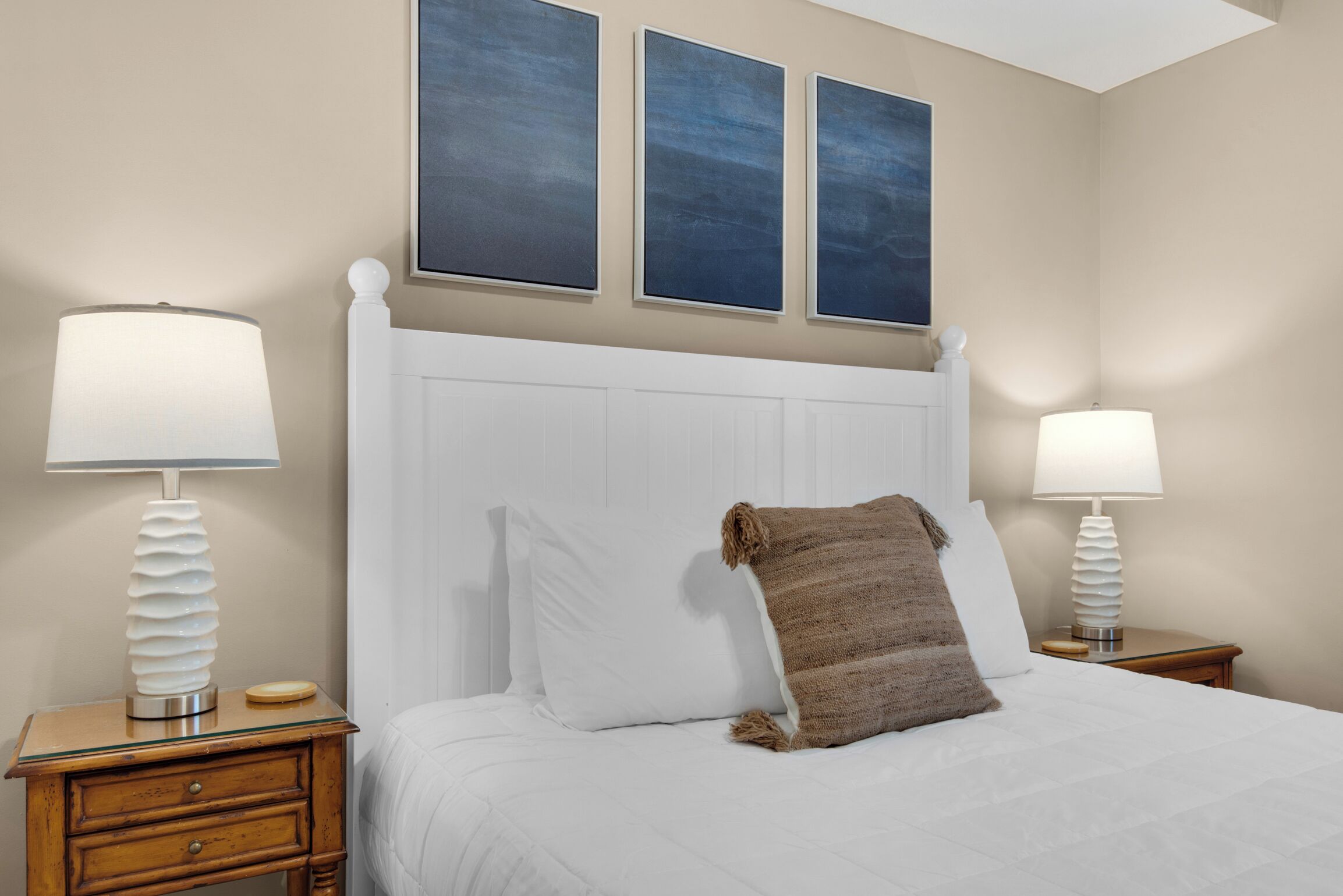 A neatly made bed with white linens, two bedside lamps, a wooden nightstand, and a brown throw blanket.