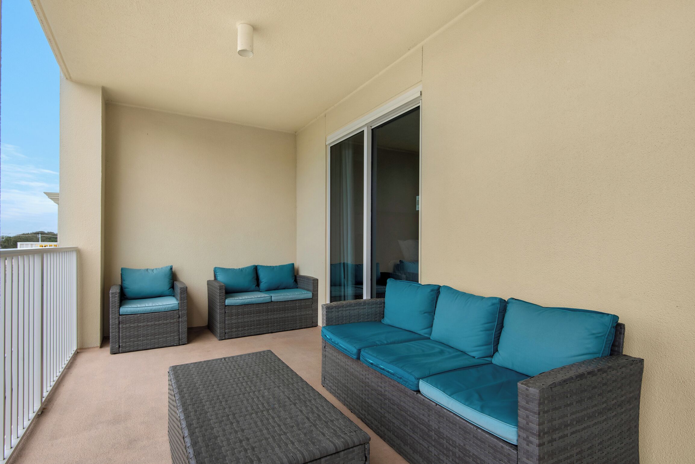 A balcony with wicker furniture, including two chairs and a sofa, and a sliding glass door.
