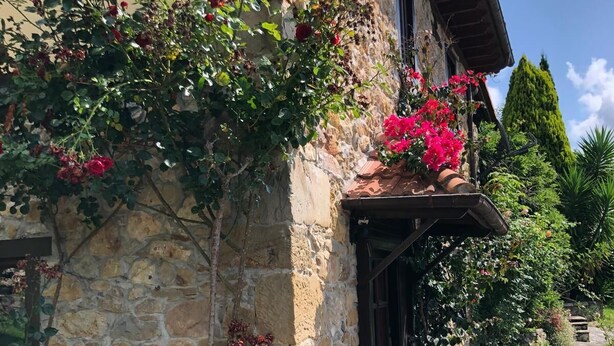Edifici de pedra amb una banca de fusta al davant, envoltat d'un camí de pedra i vegetació.