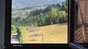 Habitació amb una finestra gran que ofereix vistes a un paisatge amb turons, arbres i una carretera.