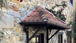 Edifici de pedra amb una porta i una finestra de fusta, una banca i un tamboret petit.