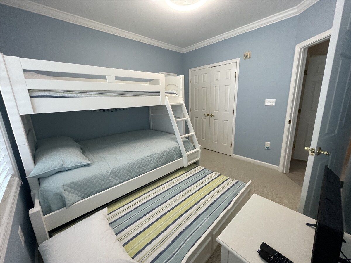 A bunk bed with a desk and chair, a door, and a light switch on the wall.