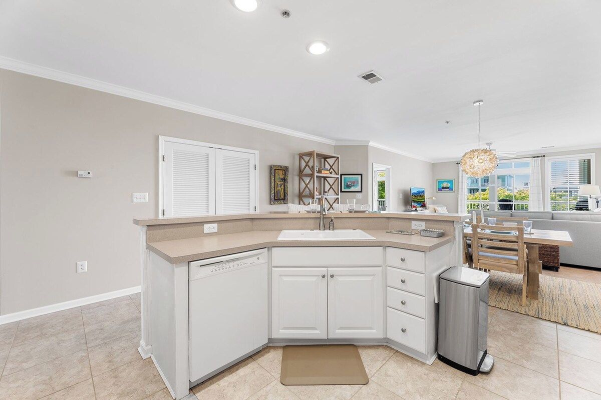 A modern kitchen with white cabinetry, a built-in dishwasher, and a stainless steel trash can.