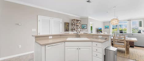 A modern kitchen with white cabinetry, a built-in dishwasher, and a stainless steel trash can.