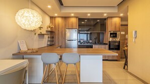 A modern kitchen with a central island, bar stools, a hanging light fixture, and built-in appliances.
