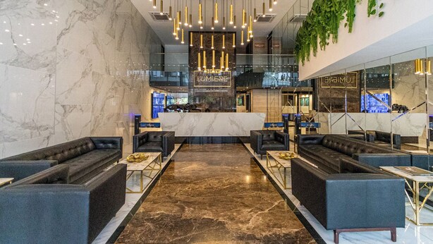 A modern lobby with a marble floor, black leather sofas, a reception desk, and a green wall with hanging plants.