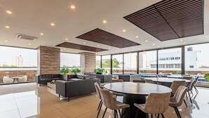 A modern lounge area with a round table, comfortable seating, and large windows offering a city view.