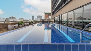 A rooftop swimming pool with a city view, modern architecture, and outdoor seating.