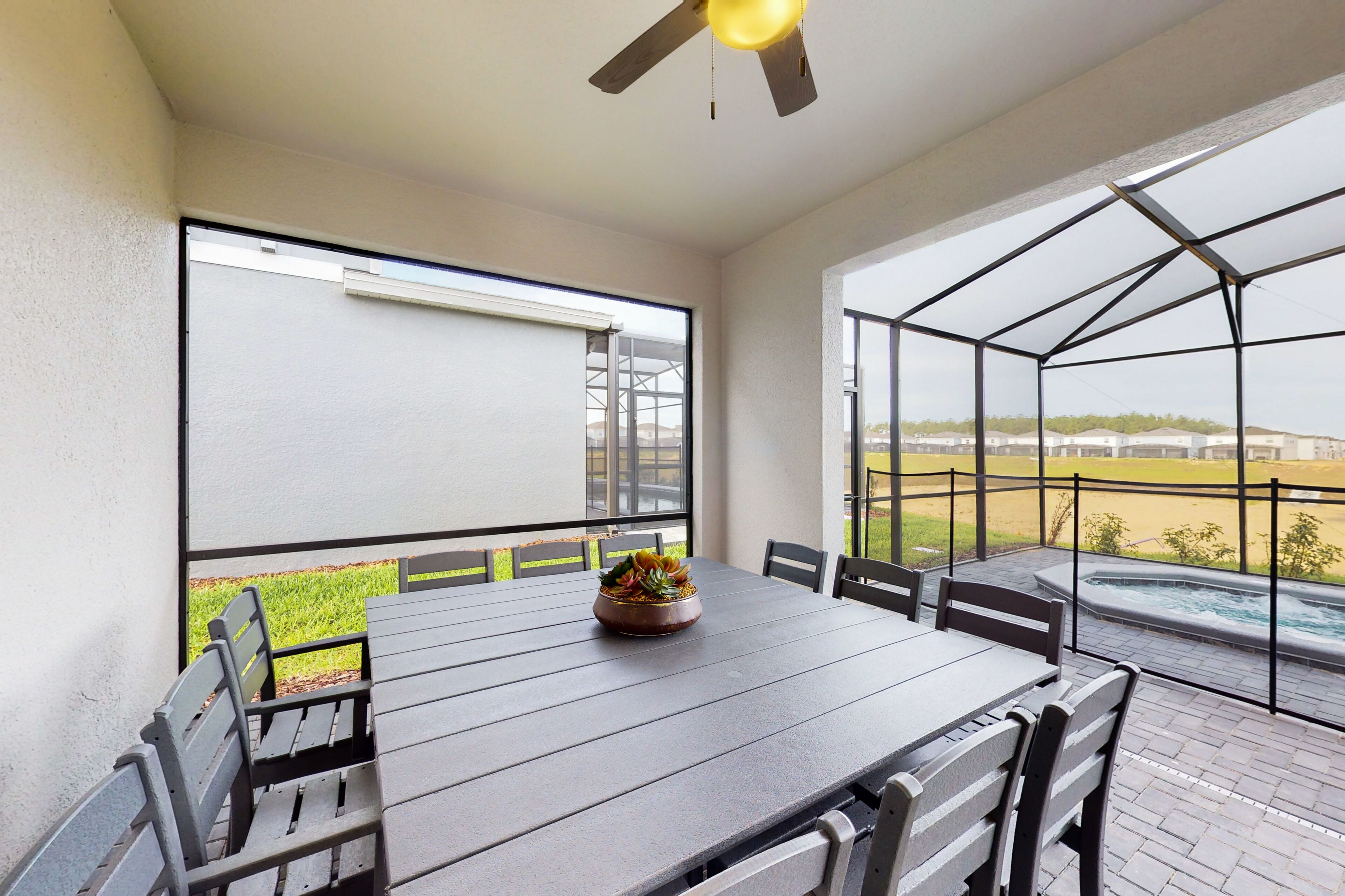 Un patio couvert avec une table et des chaises, un ventilateur de plafond et une vue sur une piscine et la verdure.