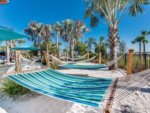 Relax in a serene beach setting with hammocks strung between palm trees and a sandy shore.