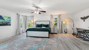 A bedroom with a bed, a desk, a chair, a ceiling fan, and a large window. - World Showcase 5 Bedrooms at Windwood Bay (Davenport)