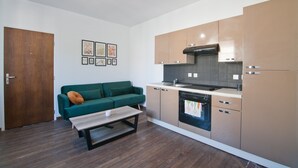 A modern kitchen with wooden cabinets, a built-in oven, and a dining area with a bench. - Le Petit St André - Appt pour 4 (Saint-André-les-Vergers)