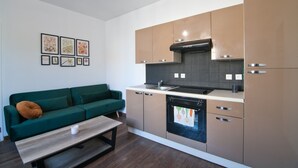 A compact kitchen with modern appliances, a green sofa, and artwork on the wall. - Le Petit St André - Appt pour 4 (Saint-André-les-Vergers)
