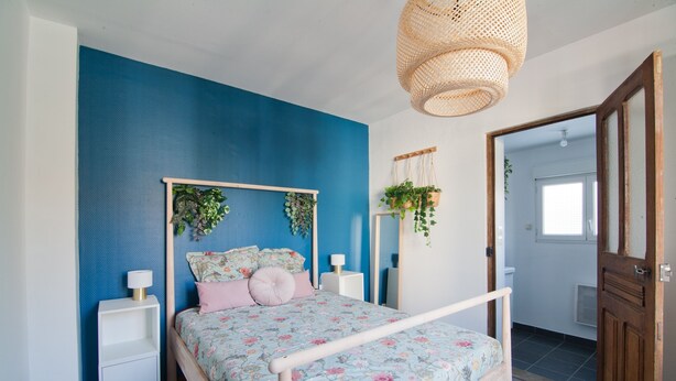 A bedroom with a bed, bedside tables, a hanging plant, and a door leading to another room. - Le Petit St André - Appt pour 4 (Saint-André-les-Vergers)
