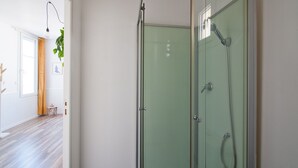 A modern bathroom with a glass shower enclosure, a wooden floor, and a small table with a plant. - L'Etudiant - charmant studio (Saint-André-les-Vergers)