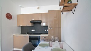 A modern kitchen with wooden cabinets, a built-in oven, and a dining table set with plates and glasses. - L'Etudiant - charmant studio (Saint-André-les-Vergers)