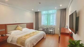 Una habitación de hotel con cama, mesita de noche, televisor, sillas y ventana con cortinas.