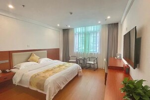 Una habitación de hotel con cama, mesita de noche, televisor, sillas y ventana con cortinas.