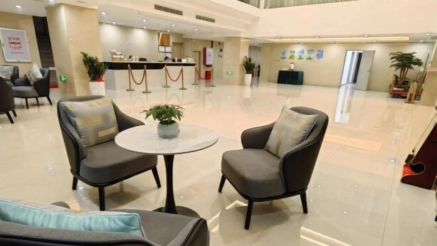 Eine geräumige Lobby mit Empfangstresen, einer Sitzecke mit Sesseln und einem kleinen Tisch sowie Topfpflanzen.