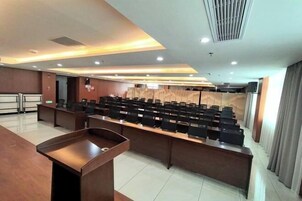 Un salón de conferencias con una mesa larga, sillas, un atril y un panel de pared de madera.