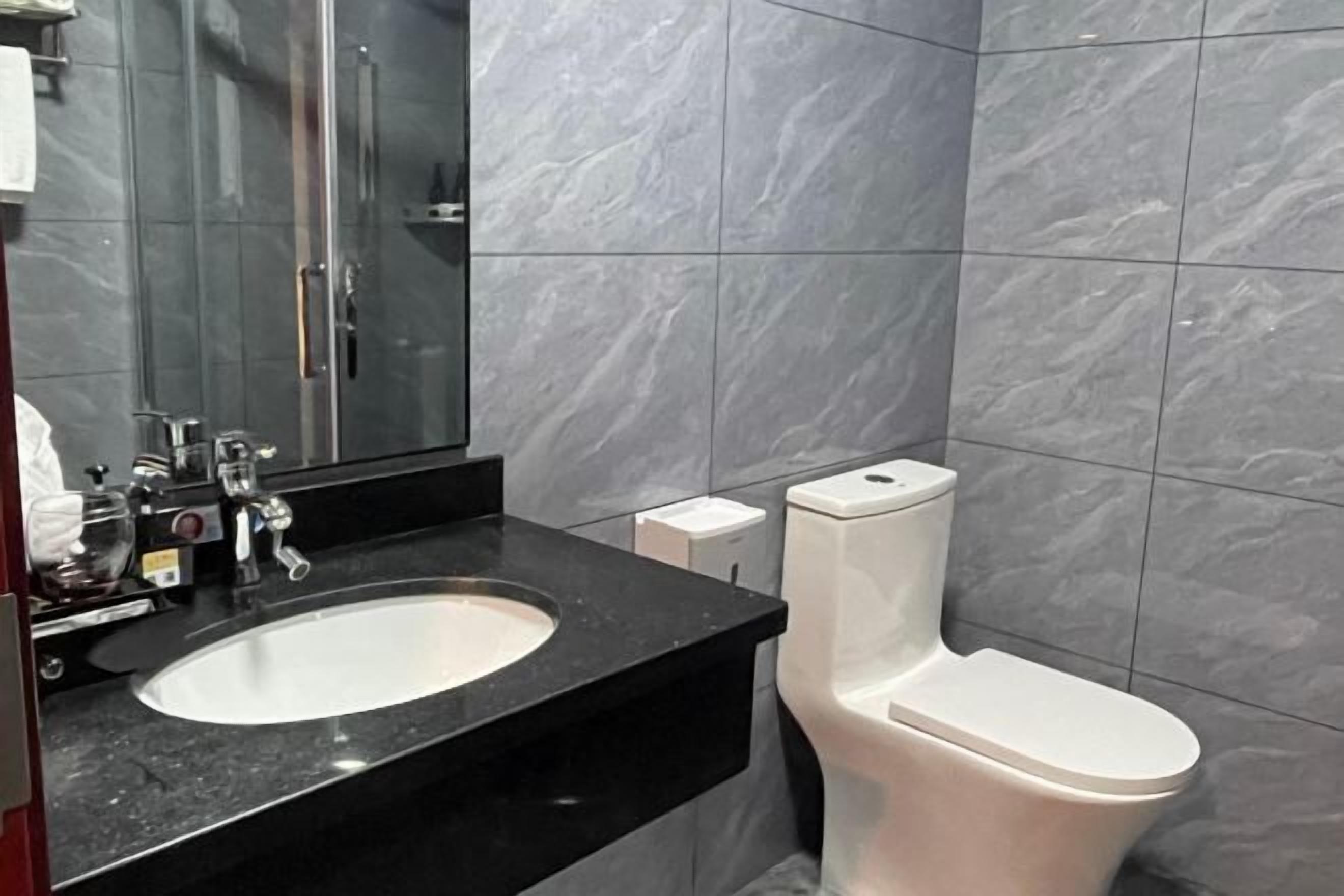 A modern bathroom with a black countertop, a white sink, and a toilet.