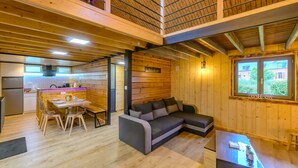 A spacious room with a wooden ceiling and walls, a dining area with a table and chairs, a sofa, and a window with a view of a house.