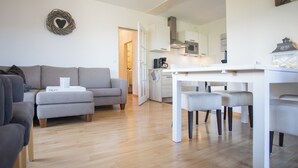 A modern living room with a grey sofa, a dining table with chairs, and a kitchen in the background.