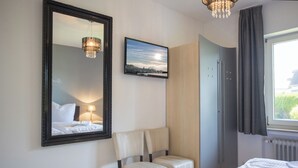 A hotel room with a bed, a chair, a mirror, a picture on the wall, and a window with curtains.
