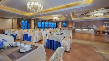A banquet hall with round tables, chairs, and a stage area.