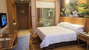 A hotel room with a bed, a desk, a chair, a TV, and a painting of a waterfall. - Vienna International Hotel (Zijin)