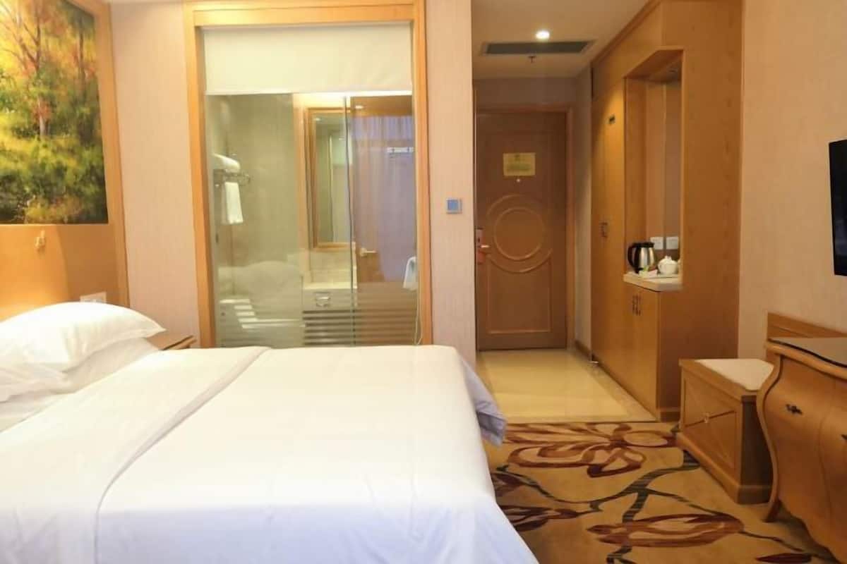 Quarto de hotel com cama, escrivaninha, cadeira e porta para um banheiro.