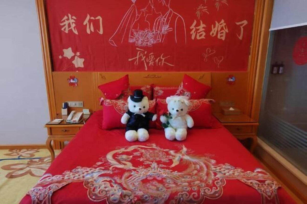 A bed with a red bedspread, two stuffed animals, and a red wall with Chinese characters.
