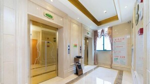 A hotel lobby with a marble floor, a reception desk, and a glass elevator. - Vienna International Hotel (Zijin)